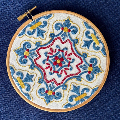 Blue, red, and yellow embroidery based on traditional Portuguese tile. Fabric is white on white cotton. Embroidery is displayed as wall art in light wood embroidery hoop.