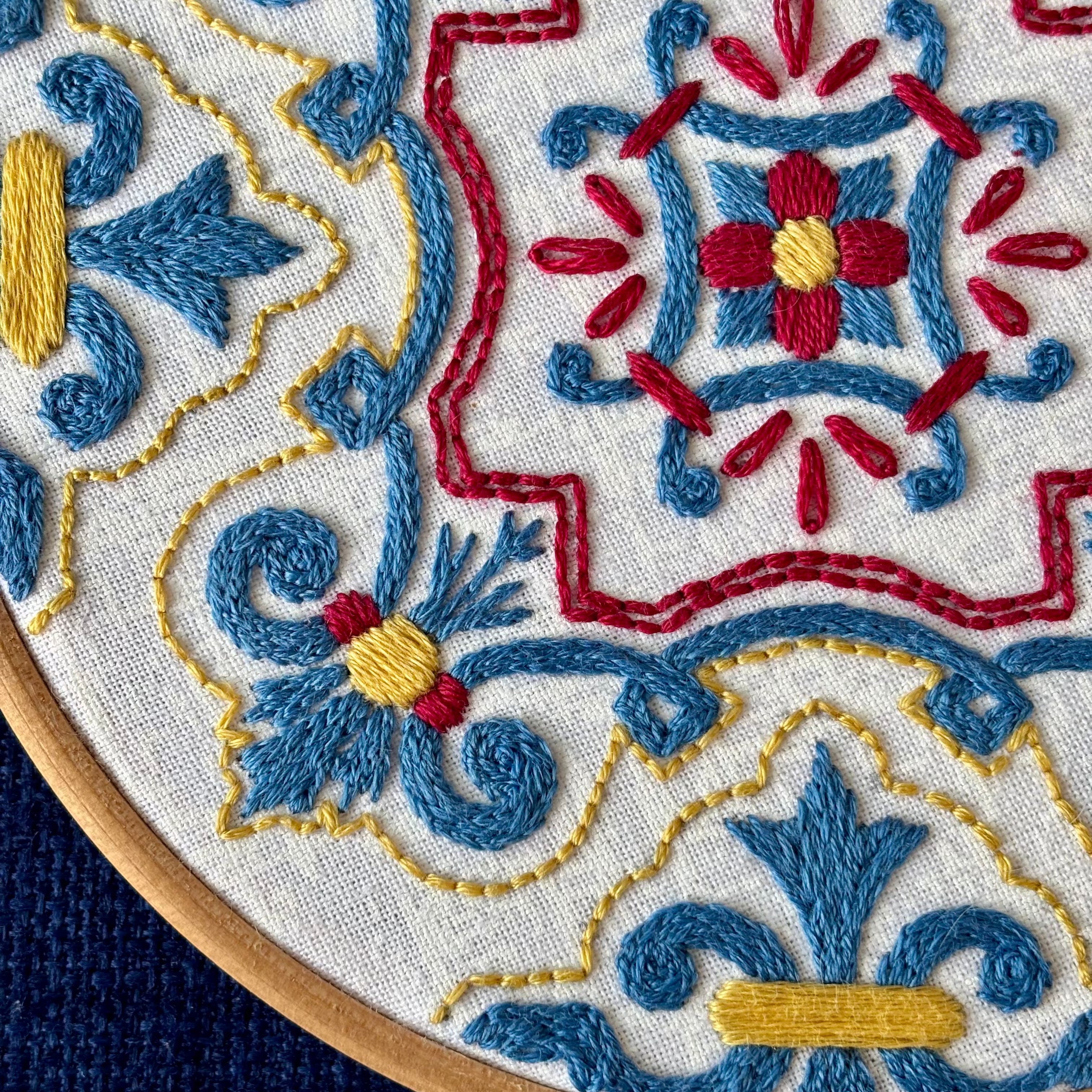 Blue, red, and yellow embroidery based on traditional Portuguese tile. Fabric is white on white cotton. Embroidery is displayed as wall art in light wood embroidery hoop.