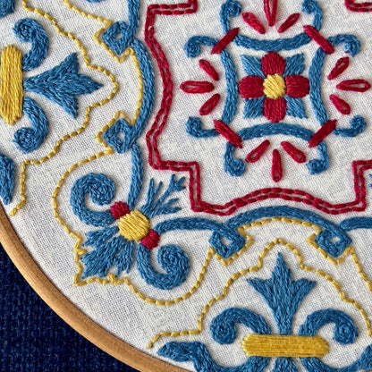 Blue, red, and yellow embroidery based on traditional Portuguese tile. Fabric is white on white cotton. Embroidery is displayed as wall art in light wood embroidery hoop.
