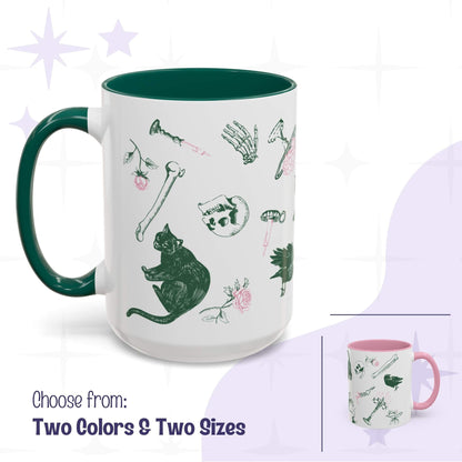 Preppy skull and bones mug shown in forest green and pink accent options with two sizes, white ceramic scattered with green and pink gothic motifs of black cats, ravens, skulls, and bones