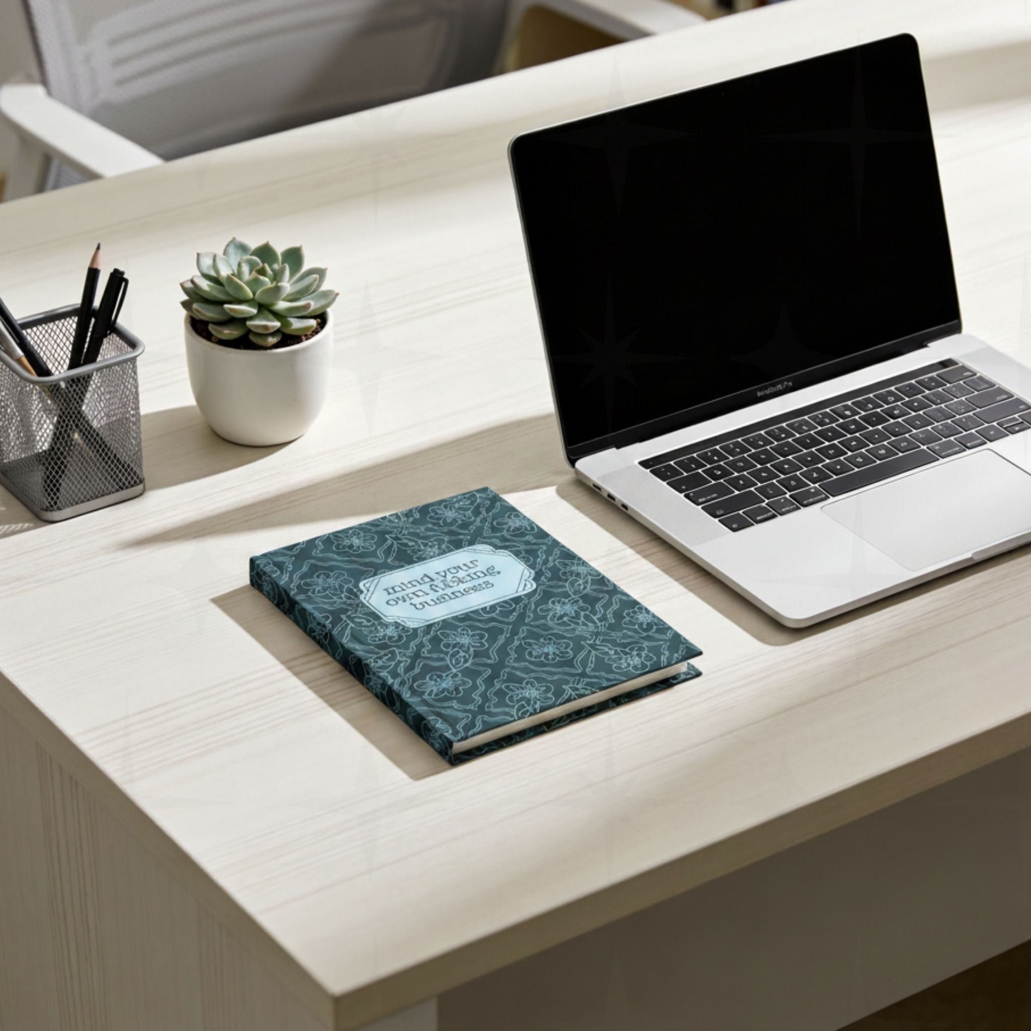 Profanity floral journal on white desk next to laptop and small succulent plant showing teal botanical hardcover