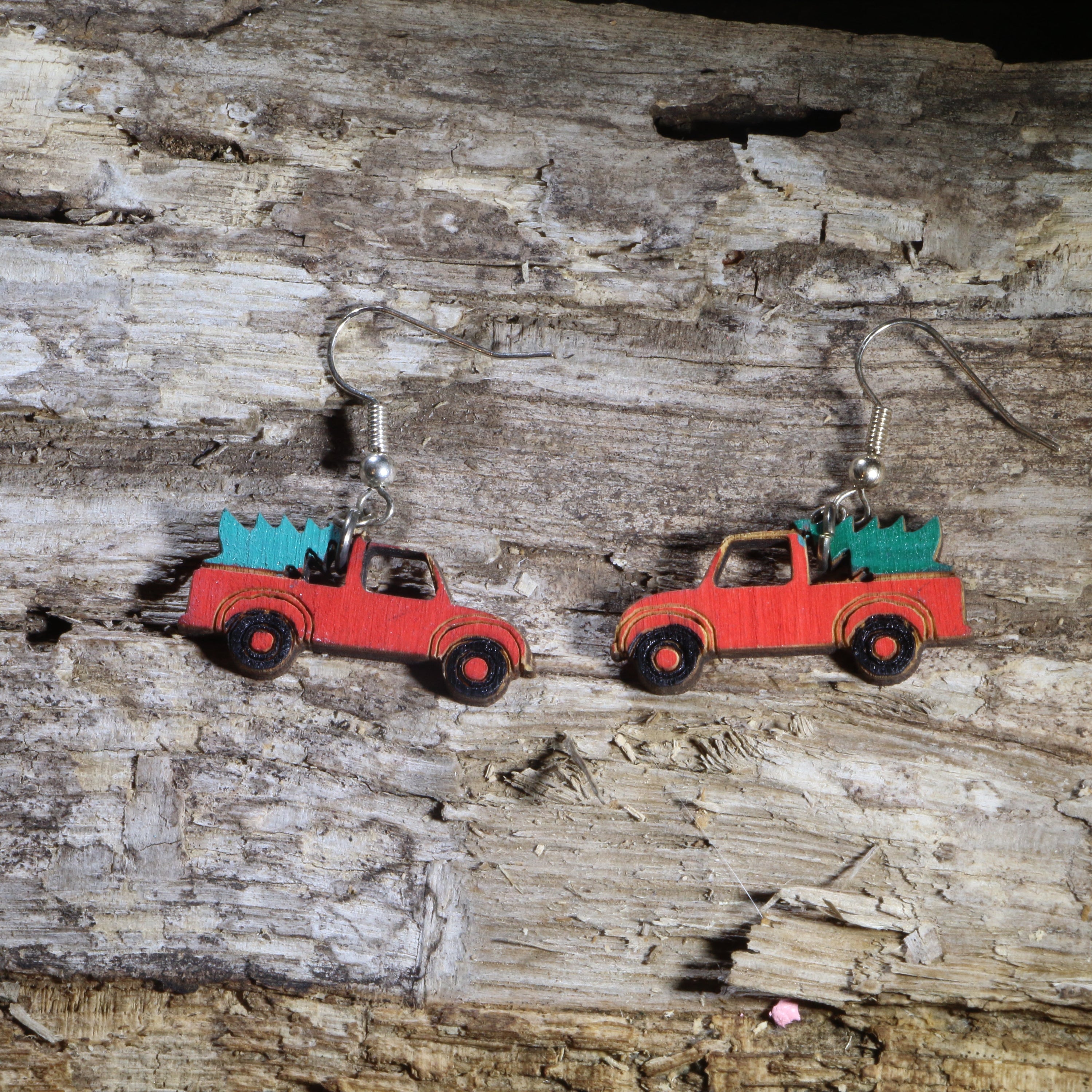 Hand-painted wooden red pickup truck dangle earrings featuring a classic vintage red truck carrying a green Christmas tree in the truck bed. Crafted from lightweight wood with hypoallergenic .925 sterling silver hooks, these festive holiday earrings are perfect for Christmas celebrations, farmhouse décor lovers, country Christmas enthusiasts, winter parties, stocking stuffers, and anyone who loves nostalgic vintage truck Christmas jewelry.