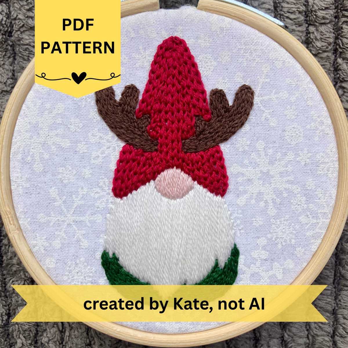 PDF pattern created by Kate, not AI. Hand embroidered Christmas gnome with a red knit hat and reindeer horns. Stitched on white cotton with sparkly white snowflakes printed on the fabric. Displayed in light wooden hoop as a DIY Christmas ornament
