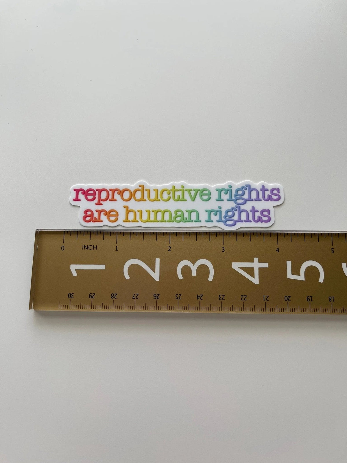Reproductive rights are human rights sticker flat lay — feminist activist laptop sticker in rainbow lettering by indie artist MangoIllustrated
