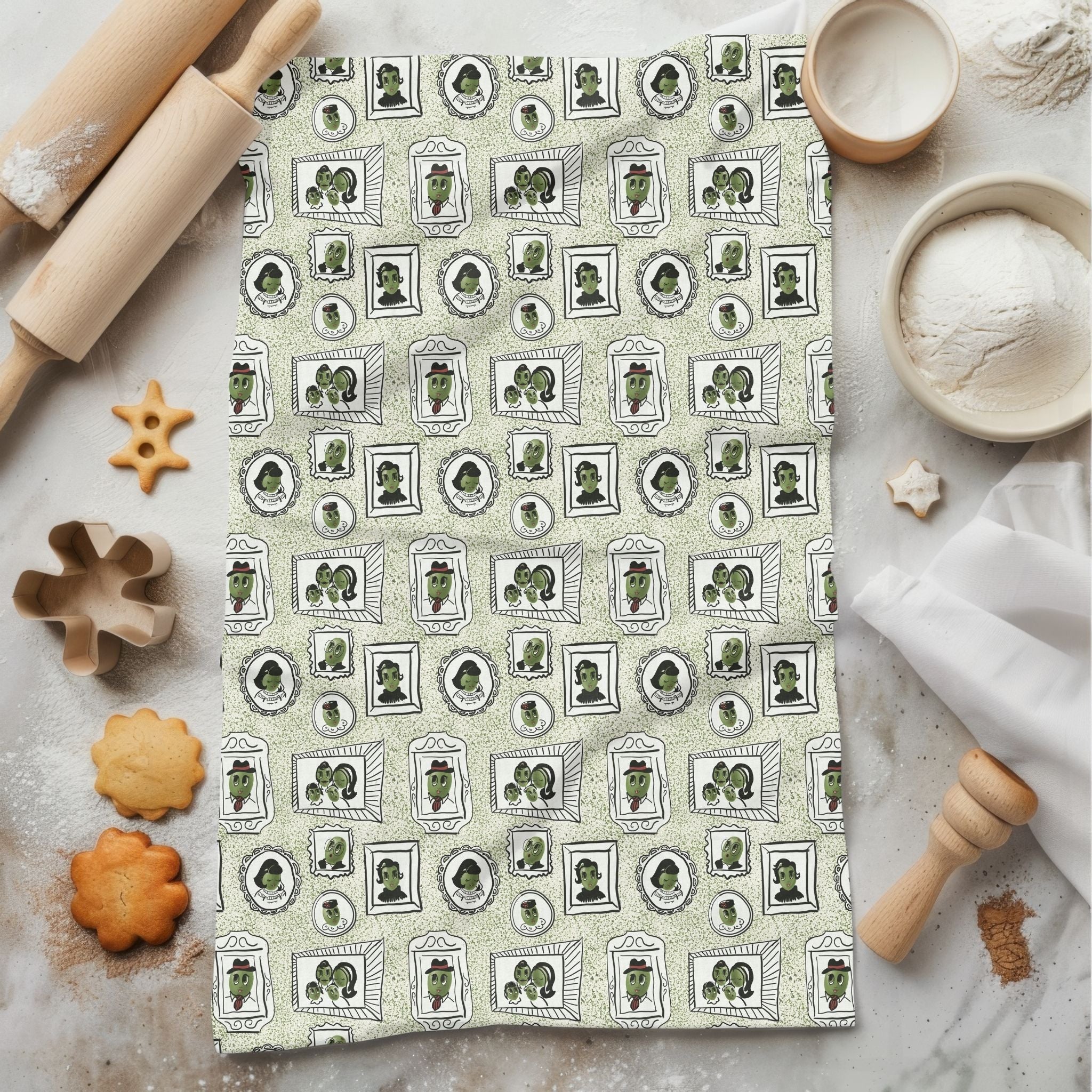 Sage green retro olive tea towel with mid-century portrait repeat pattern, styled flat on marble surface with rolling pin and cookies