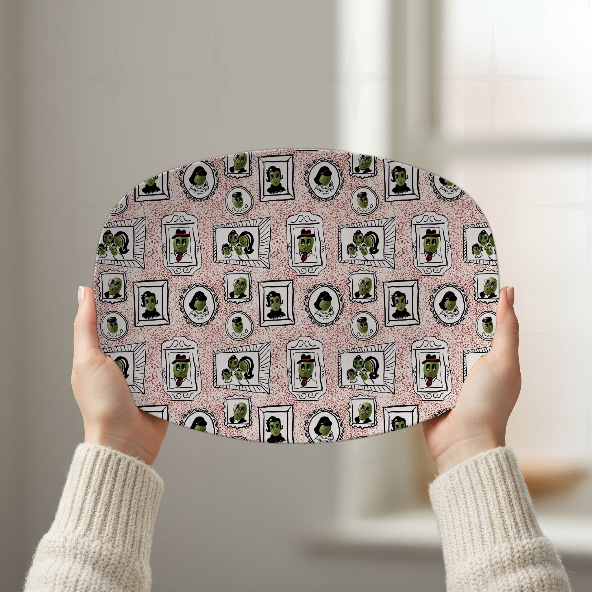 Two hands raising retro olive portrait serving platter in red colorway overhead showing full 10 by 14 inch oval gallery wall pattern in natural window light
