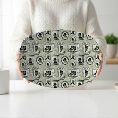 Person in cream sweater holding retro olive portrait serving platter in green colorway with both hands at white kitchen counter, full mid-century gallery wall pattern visible