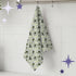 Sage green retro olive portrait tea towel hanging from silver kitchen hook against white tile backsplash