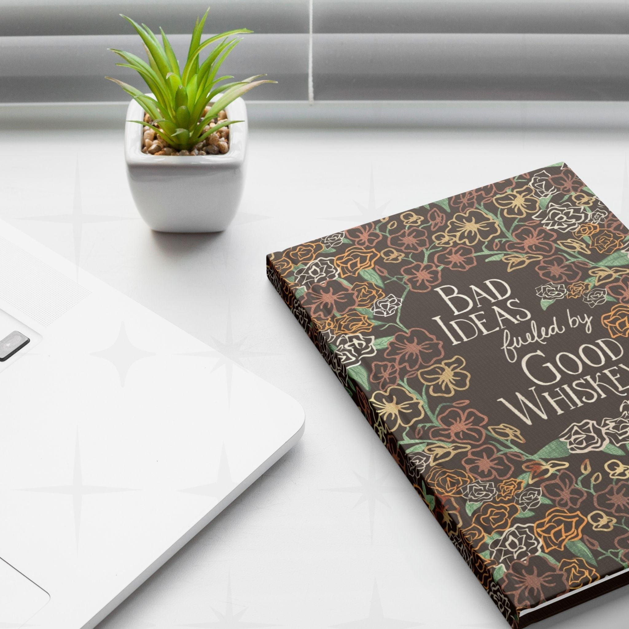Retro western maximalist floral journal closed on white desk next to laptop, pen cup, and succulent plant