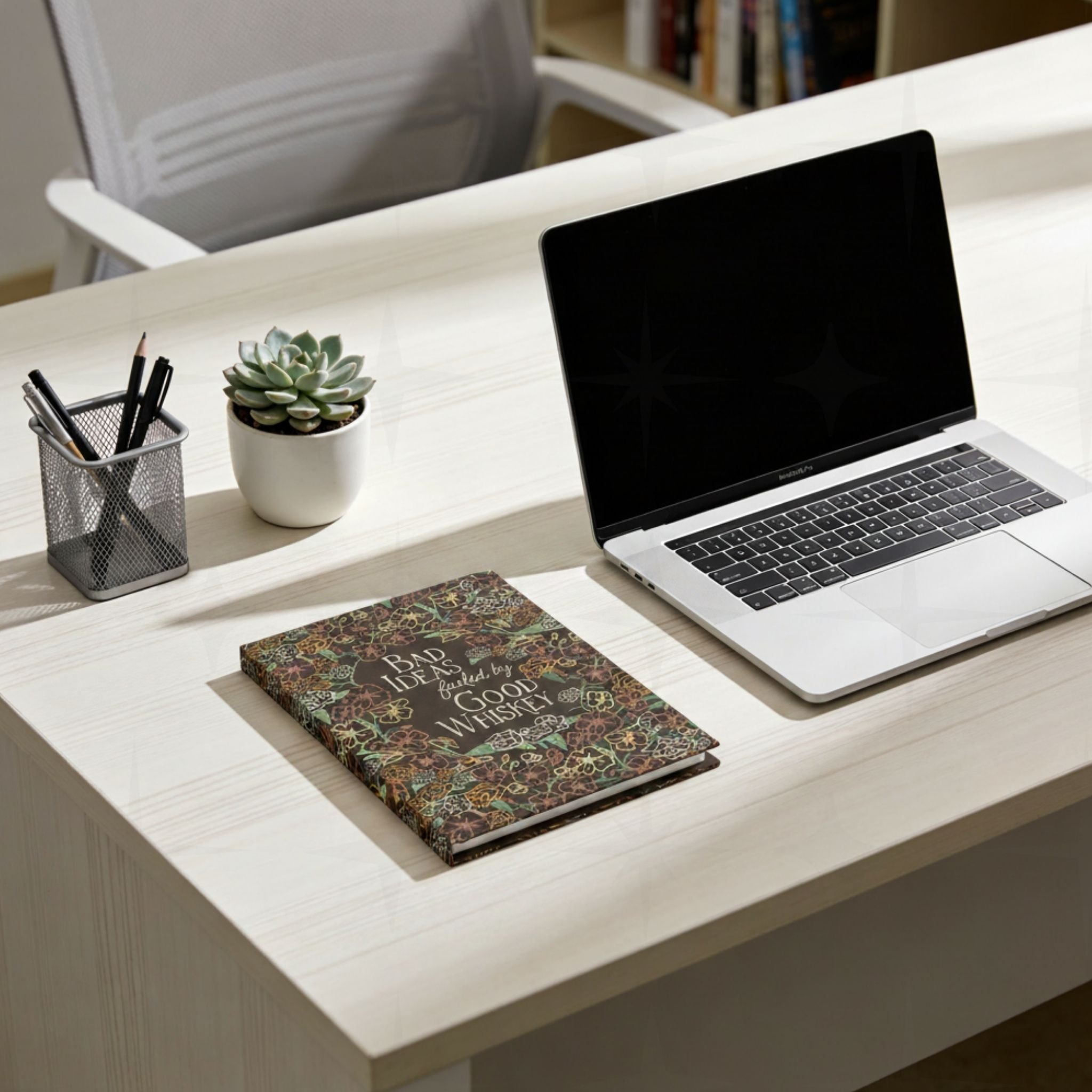 Retro western whiskey journal closed on white countertop next to laptop and small succulent, front cover visible showing wildflower pattern