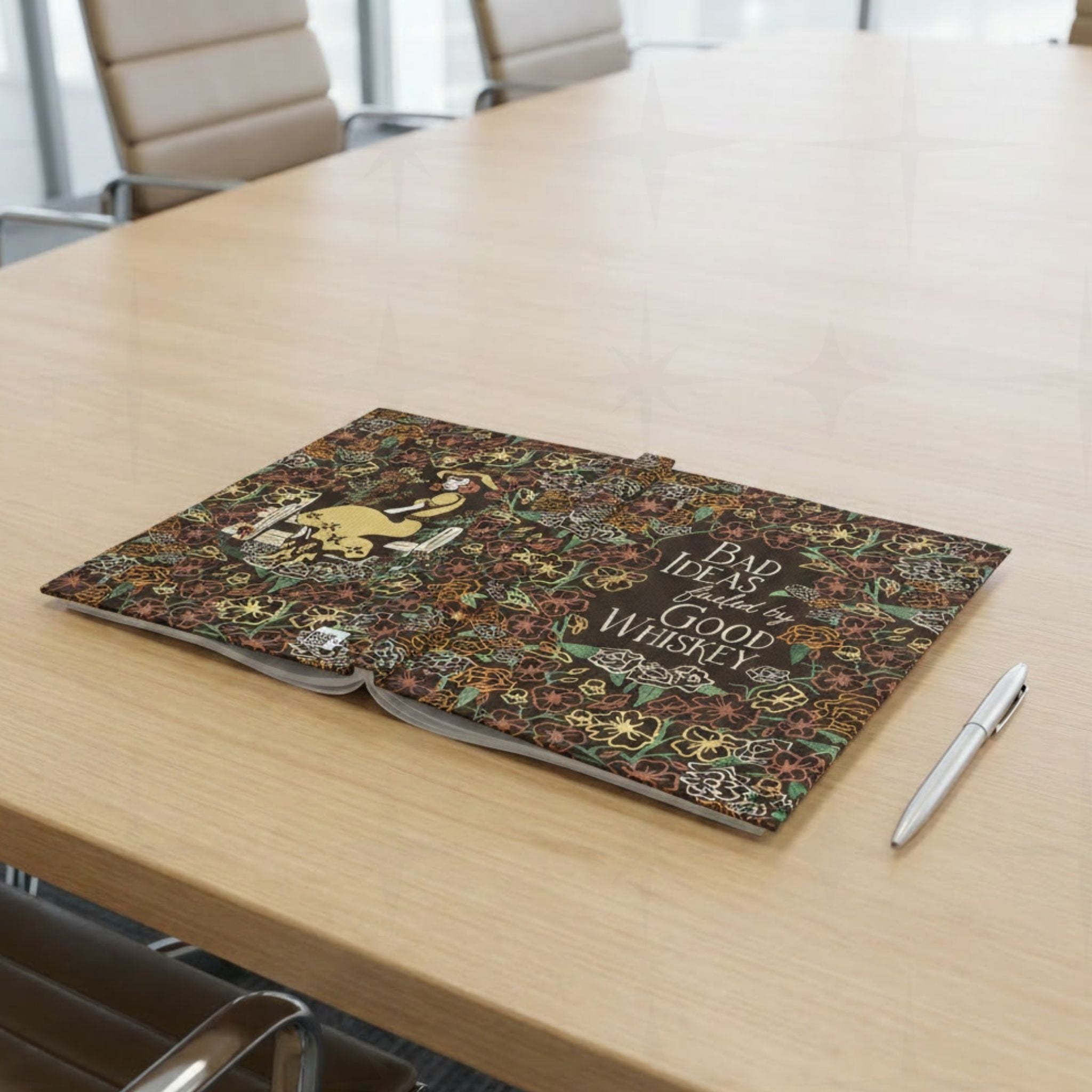 Maximalist floral cowgirl journal open flat on wooden conference table showing full wrap cover design with pen beside it