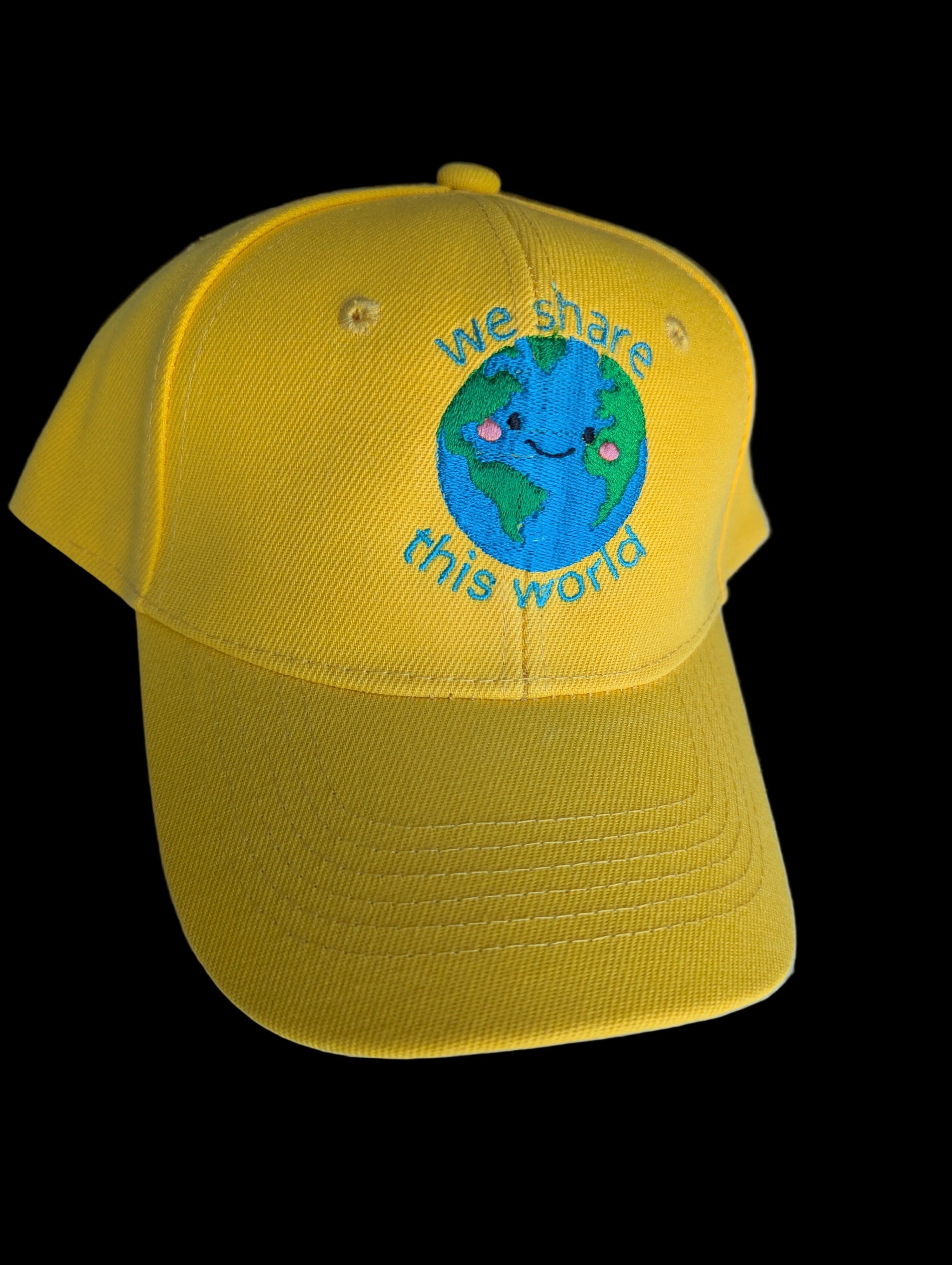 Yellow cap with a smiley Earth design that says "We Share This World" 