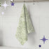 Sage green terrazzo print tea towel hanging from stainless steel rail hook on white tile kitchen wall