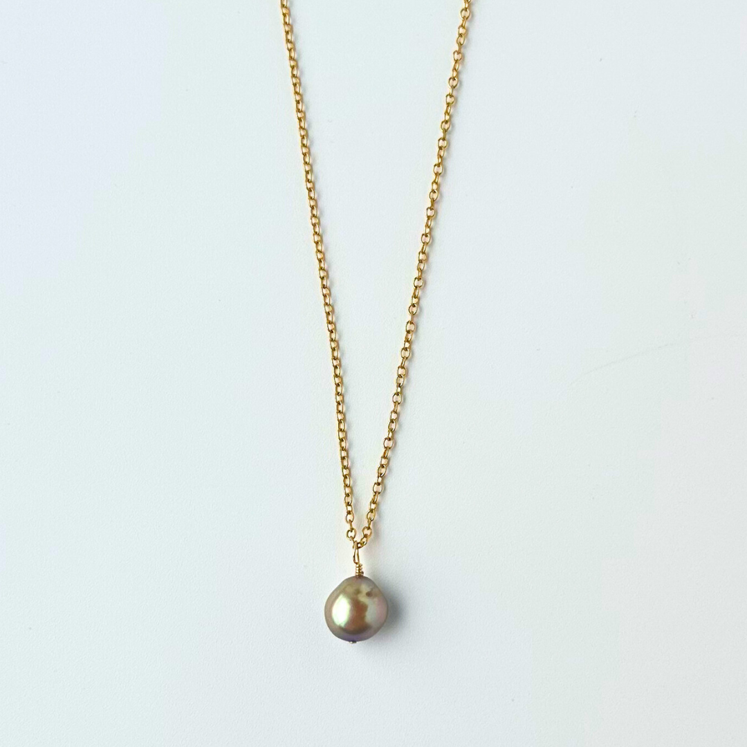 Gold necklace with a single pearl pendant on a light gray background