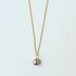 Gold necklace with a single pearl pendant on a light gray background