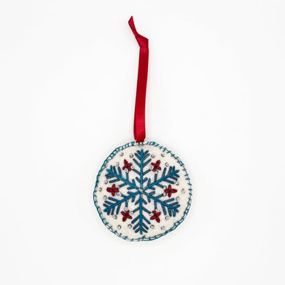 Embroidered by hand, blue red and silver snowflake design on a circular felt ornament strung with a red ribbon, ethically made by hand