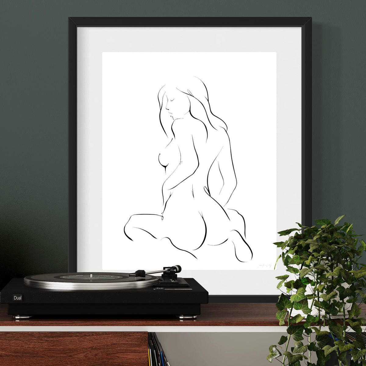 Black and white elegant illustration of sensual woman in seated pose with feminine curves; matted in black frame above oak desk and record player
