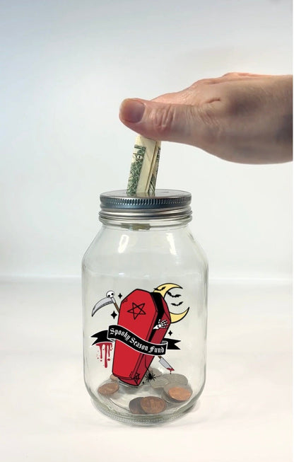 A clear glass mason jar with a silver metal lid, featuring a gothic coffin graphic, with dripping blood, moon, scythe, bats, pentagram, spider, and a moon with the text &
