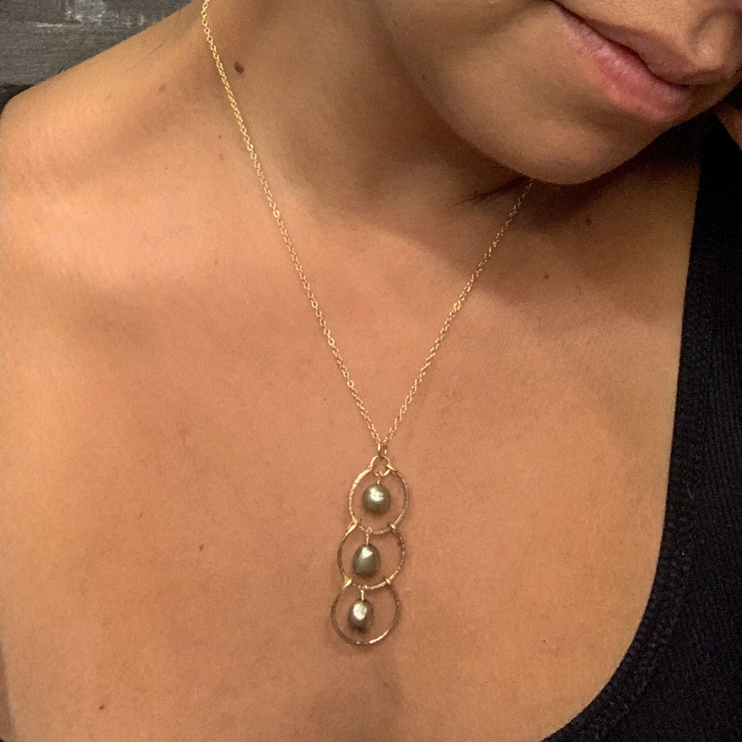 Image of necklace on model necklace is gold with three round pendants and a green pearl in the center of each