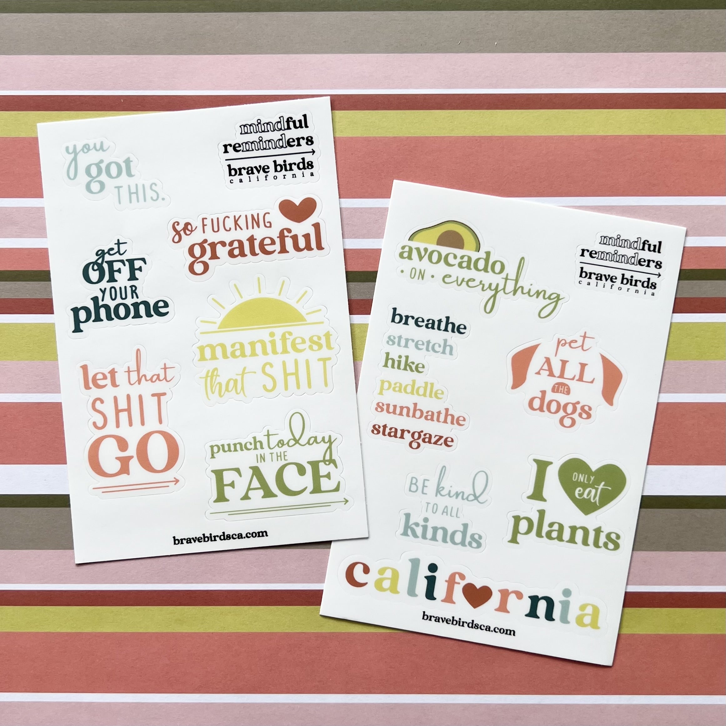 Both versions of sticker sheets, sweary and cali, layed on striped wrapping paper background