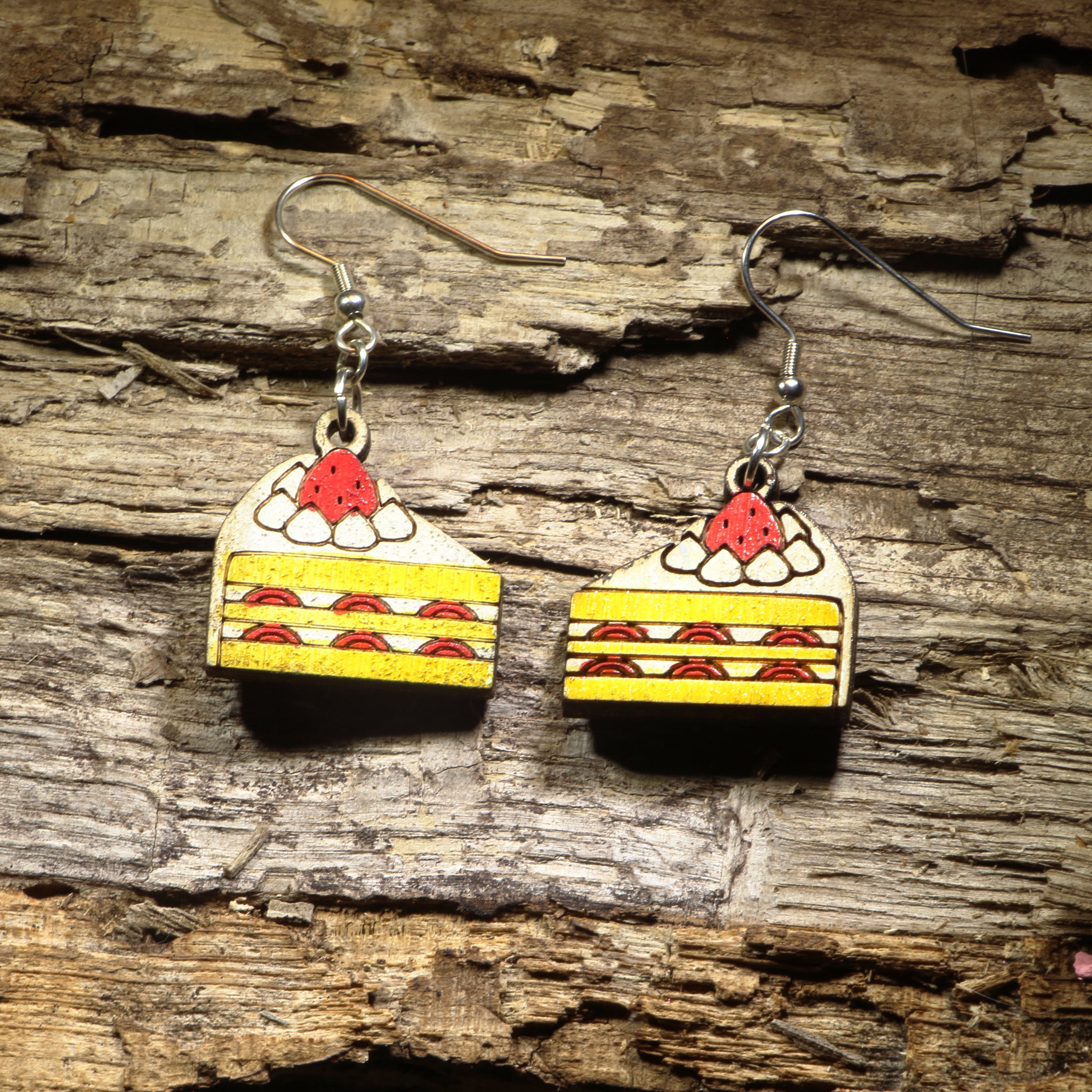 Hand-painted wooden strawberry shortcake dangle earrings featuring delicious layered strawberry cake slices topped with whipped cream and a bright red strawberry. Crafted from lightweight wood with hypoallergenic .925 sterling silver hooks, these sweet dessert earrings are perfect for bakers, pastry lovers, foodies, strawberry fans, and anyone who enjoys fun food-inspired jewelry with a whimsical touch.