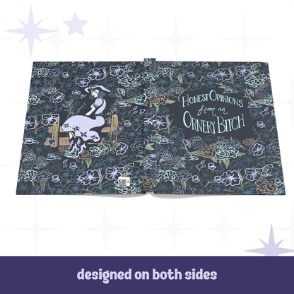 Ornery Bitch hardcover journal open flat showing full wrap design with cowgirl pinup illustration on back cover and hand-lettered text on front, dark floral pattern across both sides