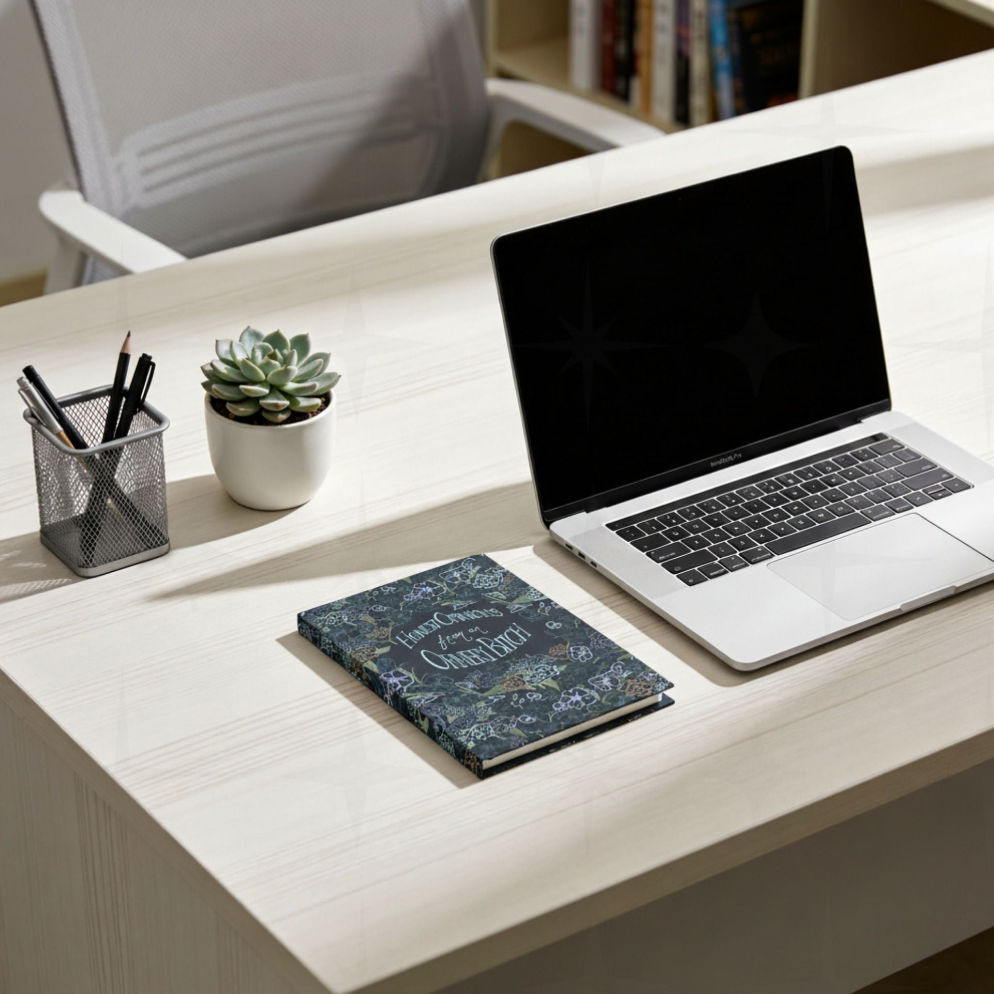 Dark floral ornery bitch hardcover journal on modern office desk next to laptop, pens, and succulent plant in bright workspace