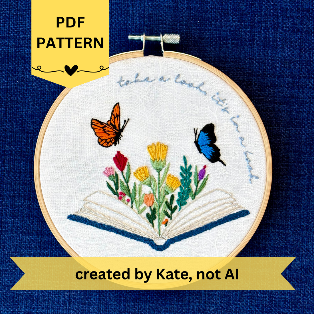 PDF pattern created by Kate, not AI. Photo of a hand embroidered design inspired by Reading Rainbow. Fabric is white cotton with white flowers printed on it. There is an open book with a rainbow of flowers growing from it. Hovering above are an orange and black butterfly and a bright blue and black butterfly. The top right curve of the pattern reads, "take a look, it&