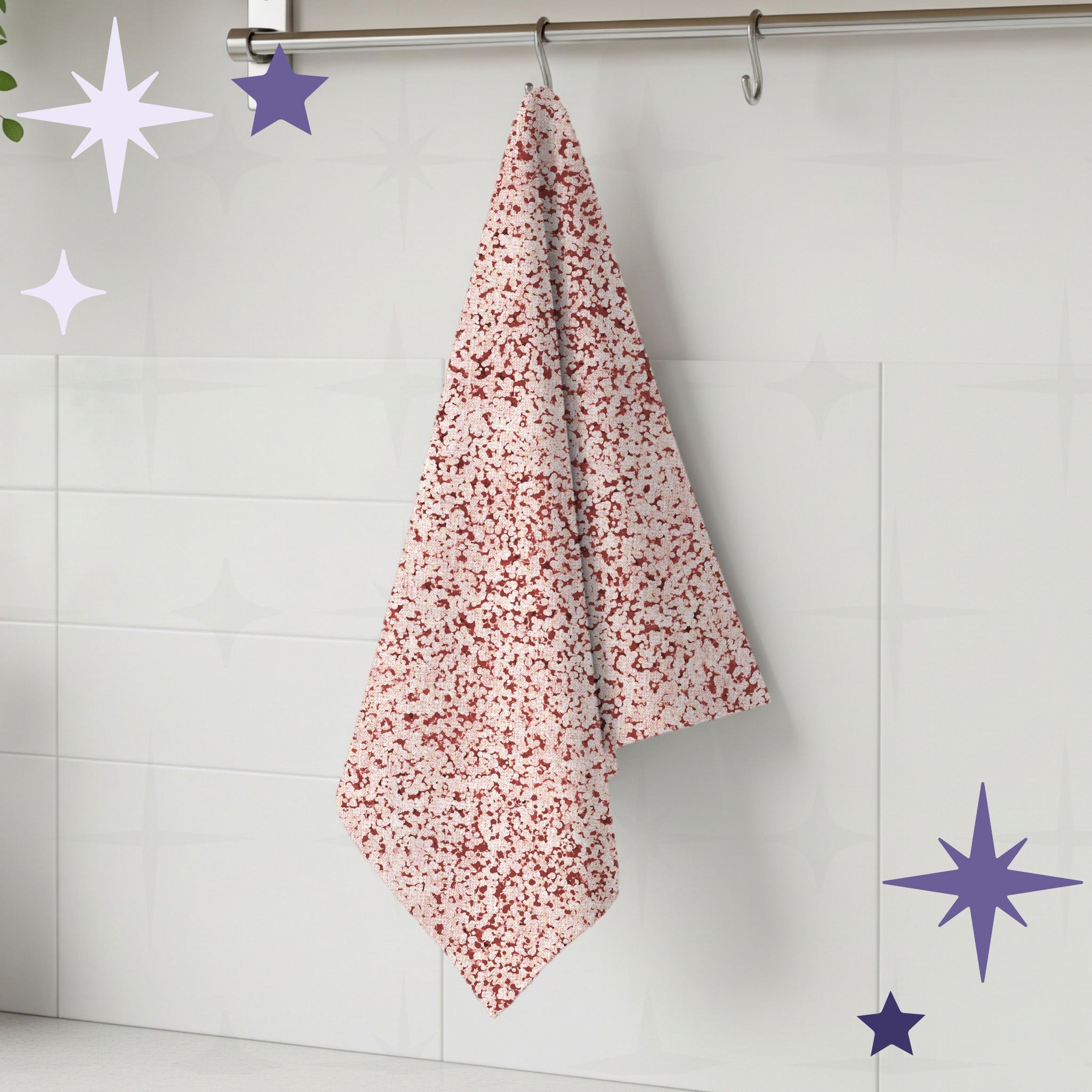 Terracotta red terrazzo print kitchen towel hanging from stainless steel rail hook on white tile kitchen wall