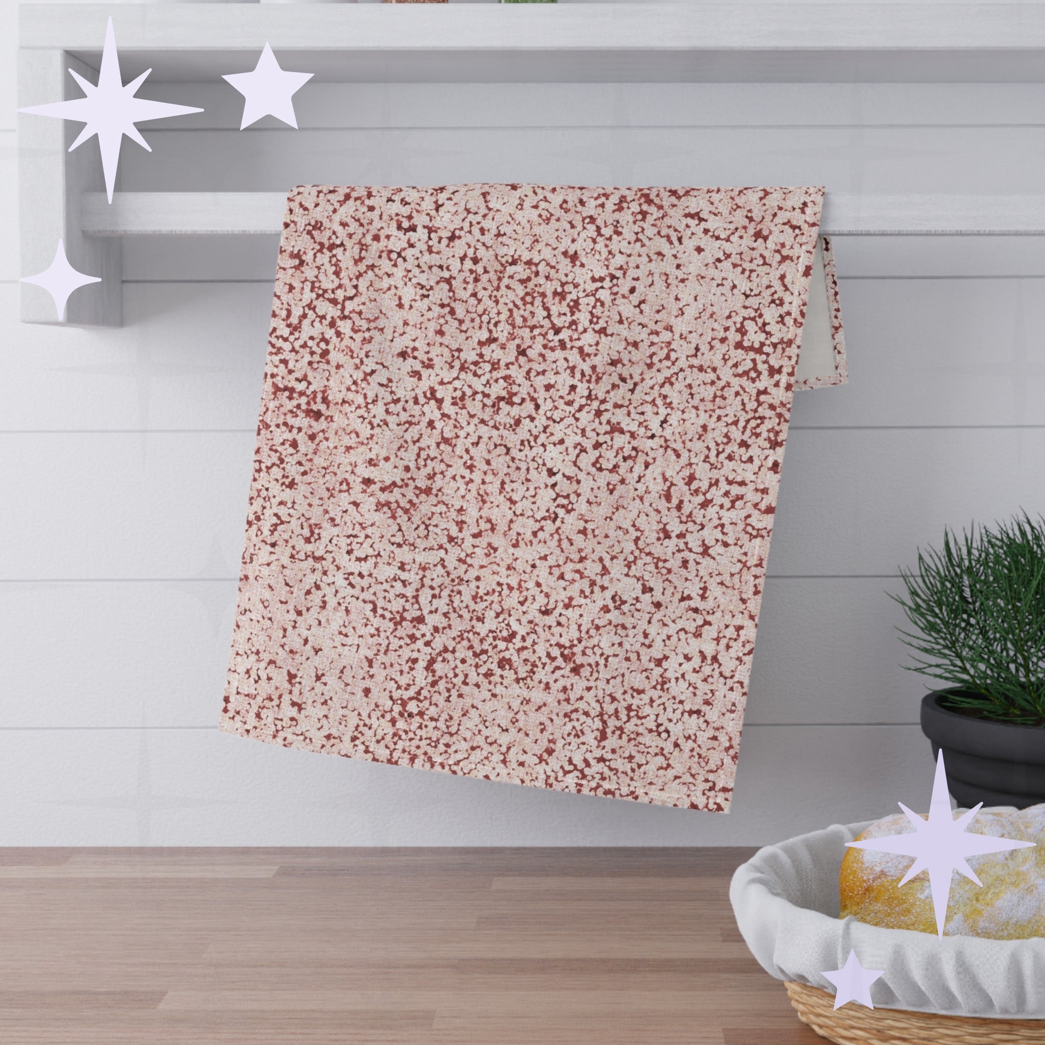 Terracotta red terrazzo tea towel folded and draped over white shaker shelf rail in kitchen setting with pine plant and bread basket