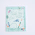 A folded greeting card with a colorful design featuring sewing-related images such as scissors, thread, and fabric, with the text &