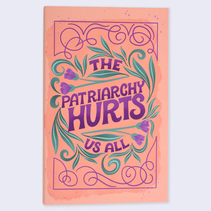 A flat lay image of a notebook with an orange cover featuring a purple-colored floral and text design, with the title &