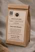 A brown kraft paper coffee bag standing upright on a soft gray fabric surface. The front label reads &