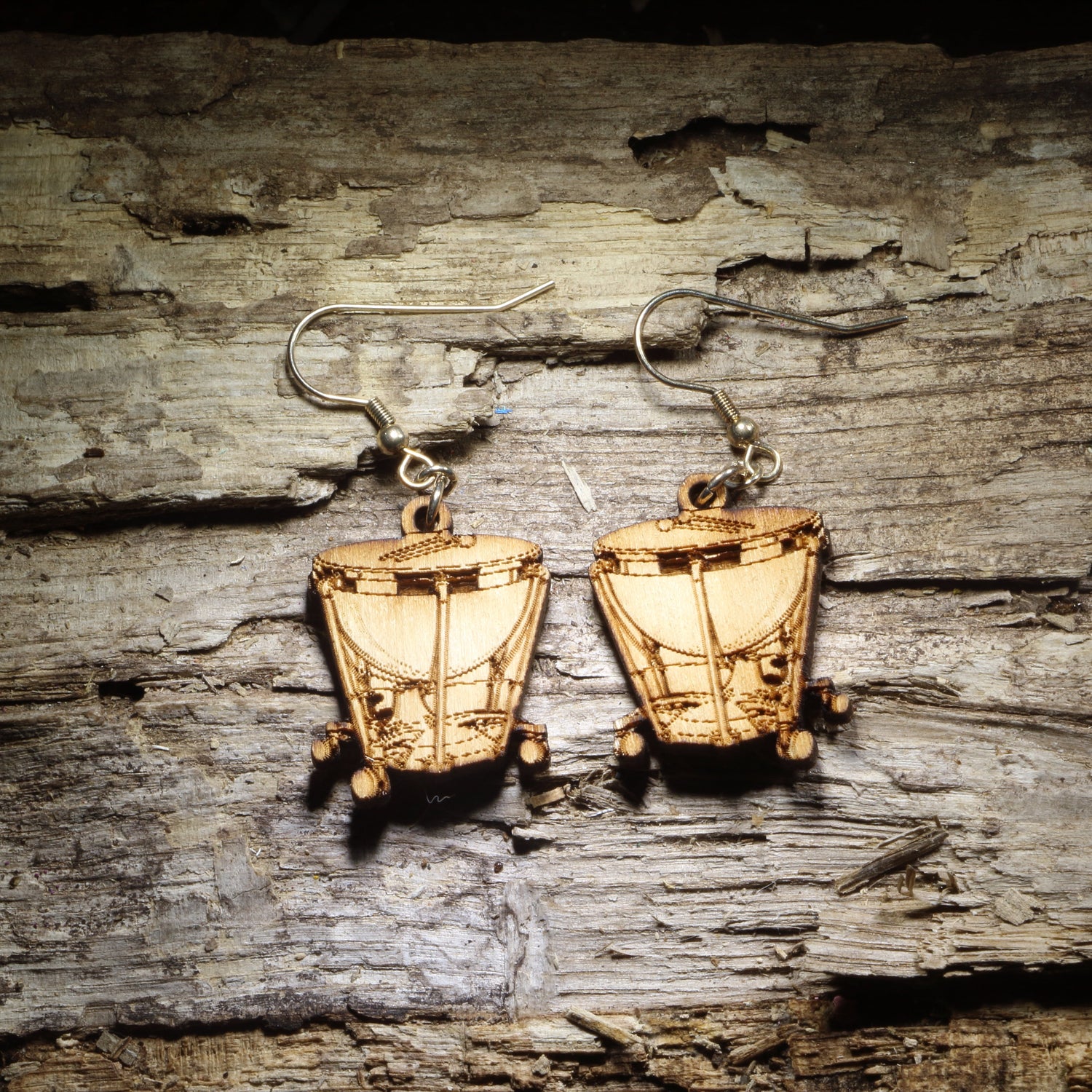 Pair of natural wood timpani kettle drum dangle earrings with detailed percussion instrument design displayed on rustic weathered wood