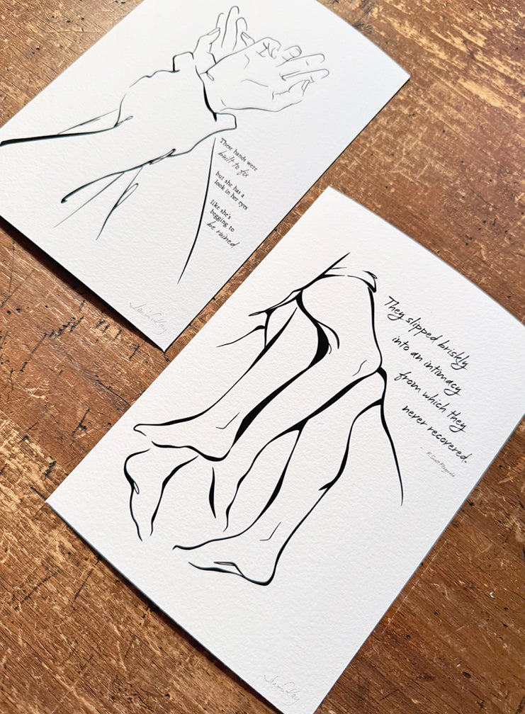 Fine art prints of "Together" and "I Got You," printed on Aquarelle Rag paper, laying on a wood desk; both are pieces from Jennifer Kay&