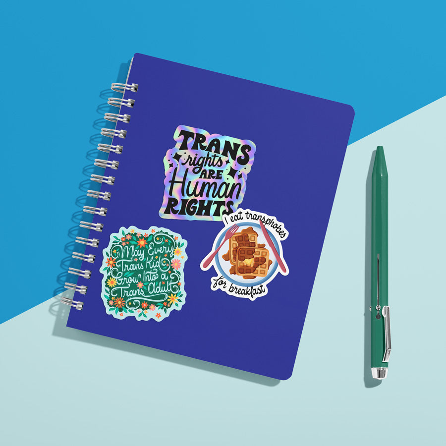 A notebook with three trans rights stickers on the cover