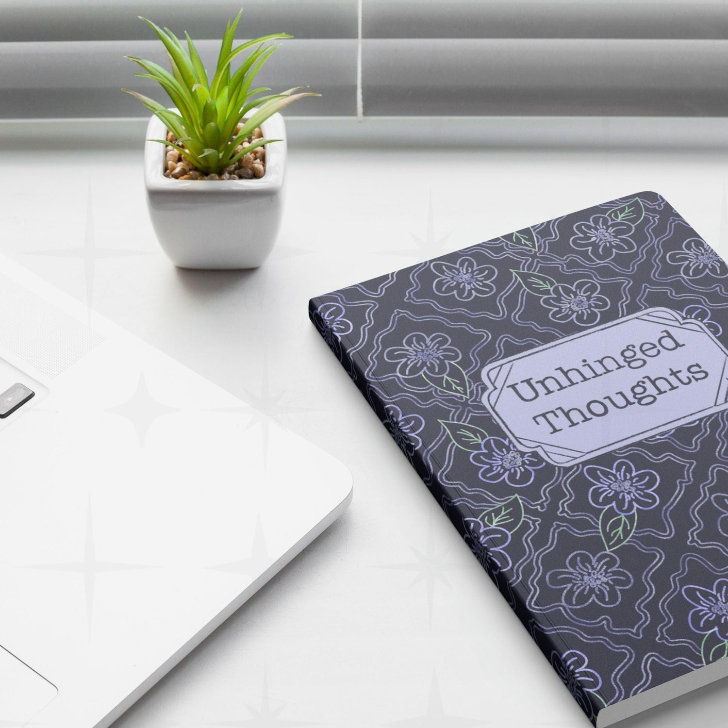 Unhinged Thoughts dark floral softcover journal placed on a desk next to a laptop and a plant