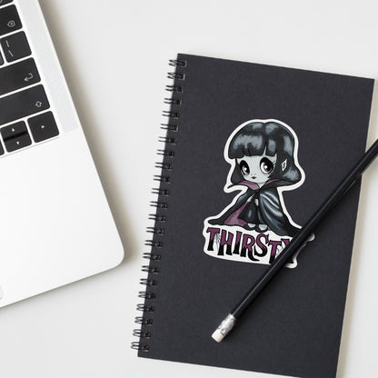Chibi vampire girl sticker on a black spiral notebook beside a laptop and pencil