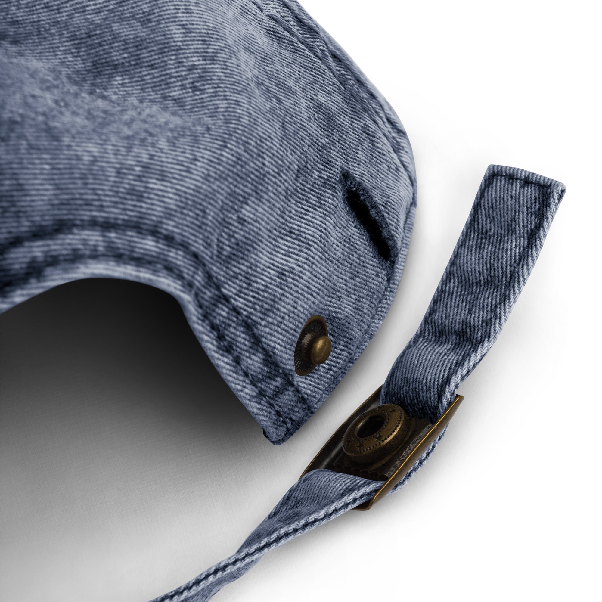 Close-up of faded blue cotton dad hat strap with brass buckle and distressed fabric detail on white background
