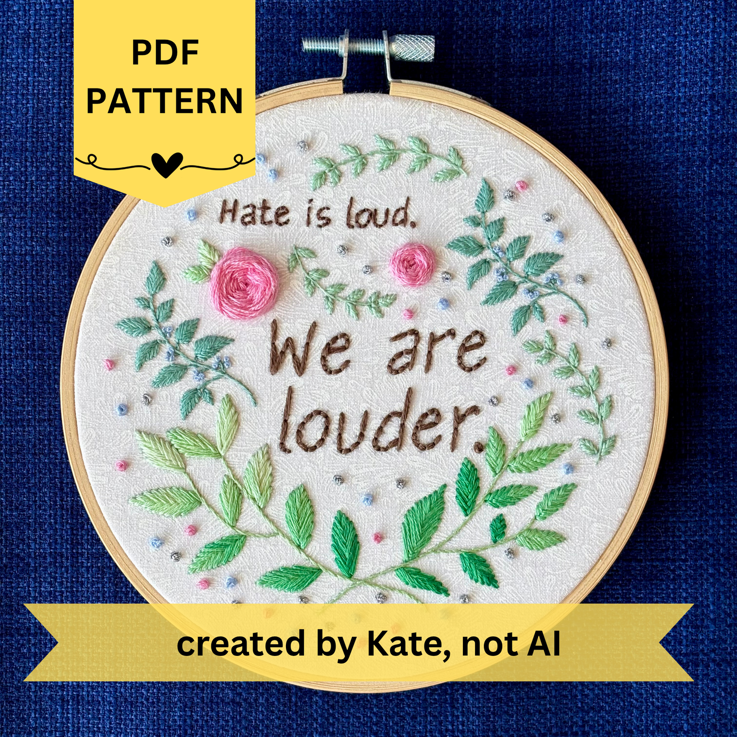 PDF pattern created by Kate, not AI. "Hate is loud. We are louder." Pride quote hand embroidered in chocolate brown. Surrounded by green leaves &amp; vines, with pink roses, blue berries, &amp; metallic silver dots. Sewn on white-on-white cotton. Framed in light wood embroidery hoop as wall art.