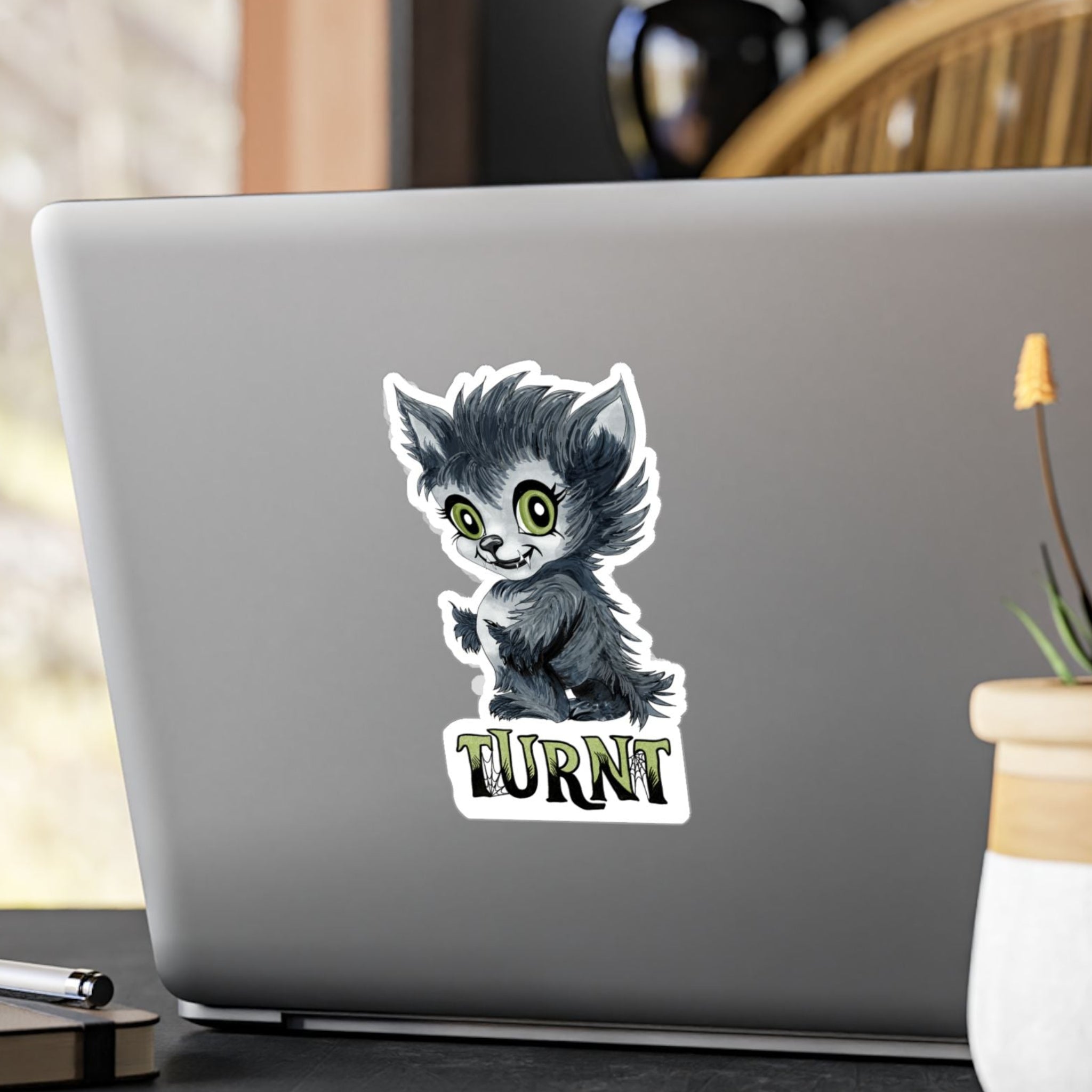 Medium chibi werewolf sticker with green eyes and TURNT lettering on the back of a silver laptop