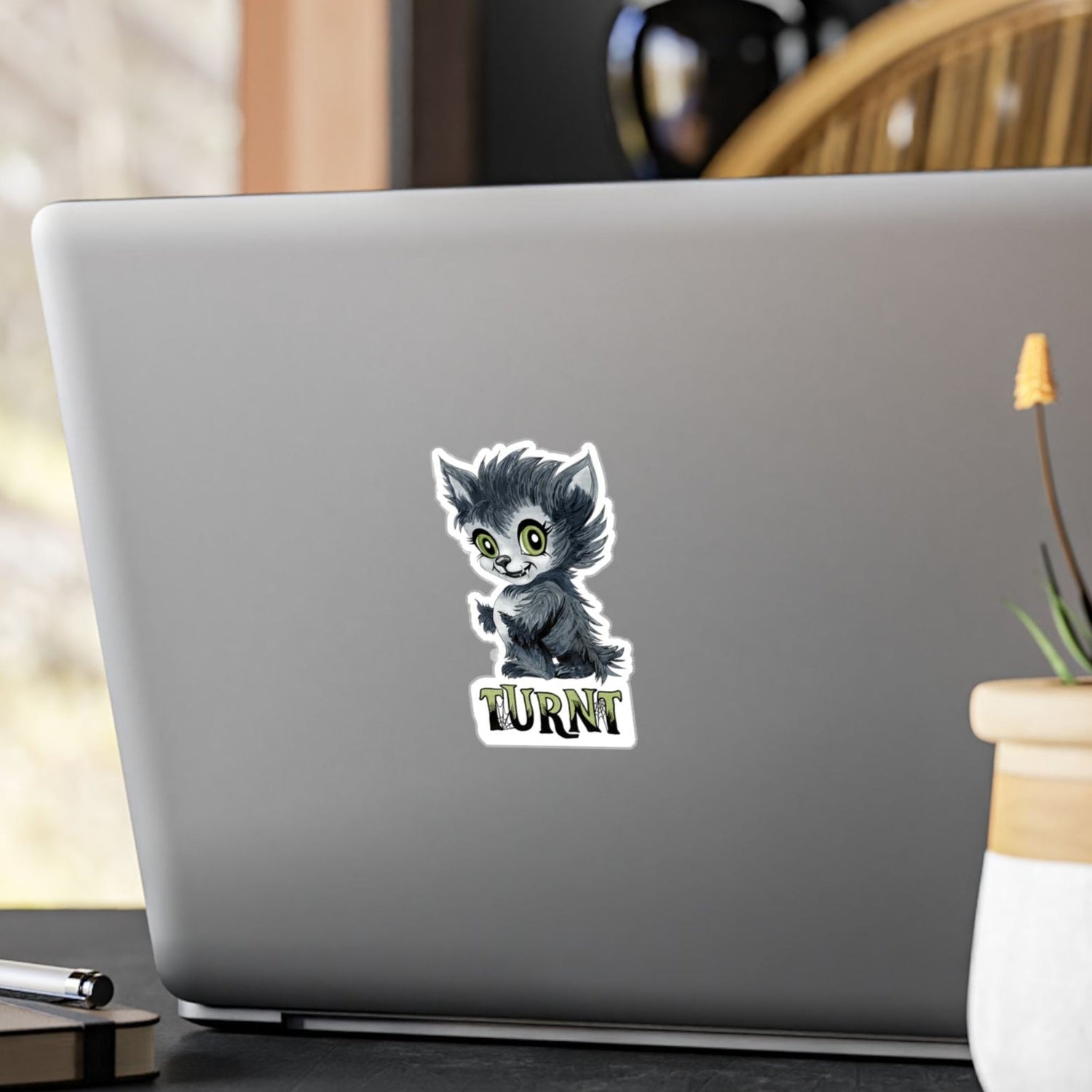 Small chibi werewolf sticker with green eyes and TURNT lettering on the back of a silver laptop