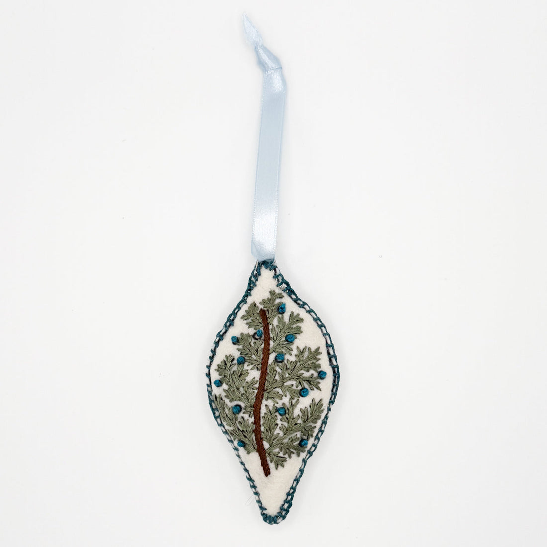 Hand embroidered and sewn oblong Christmas ornament with a brown branch, greenery and blue berries, ethically made by syrian refugee women, lay flat