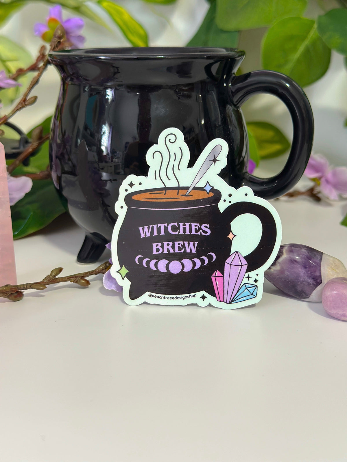 A die-cut sticker featuring a black cauldron with purple text reading &