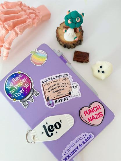 A purple notebook or journal decorated with various whimsical and spooky stickers, including a &
