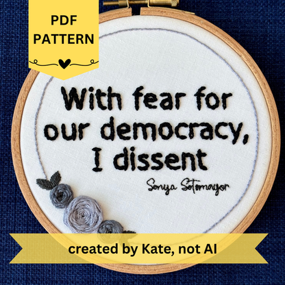 PDF Pattern created by Kate, not AI. "With fear for our democracy, I dissent. Sonia Sotomayor" Quote hand embroidered in a strong sans-serif font in black embroidery thread. A floral wreath of light and medium gray roses surrounds the text. Fabric is white cotton. Embroidery is displayed as wall art in a wood embroidery hoop.